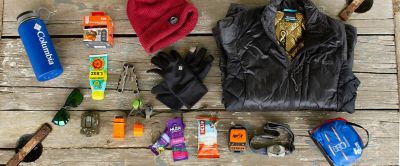 The Ten Essentials of the Backcountry are pictured laid out on a wooden camp table.